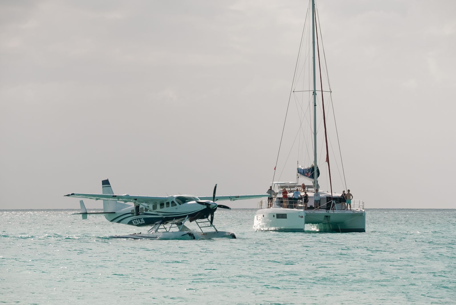 The Cessna Seaplane at rest on turquoise water beside a catamaran, guests on deck