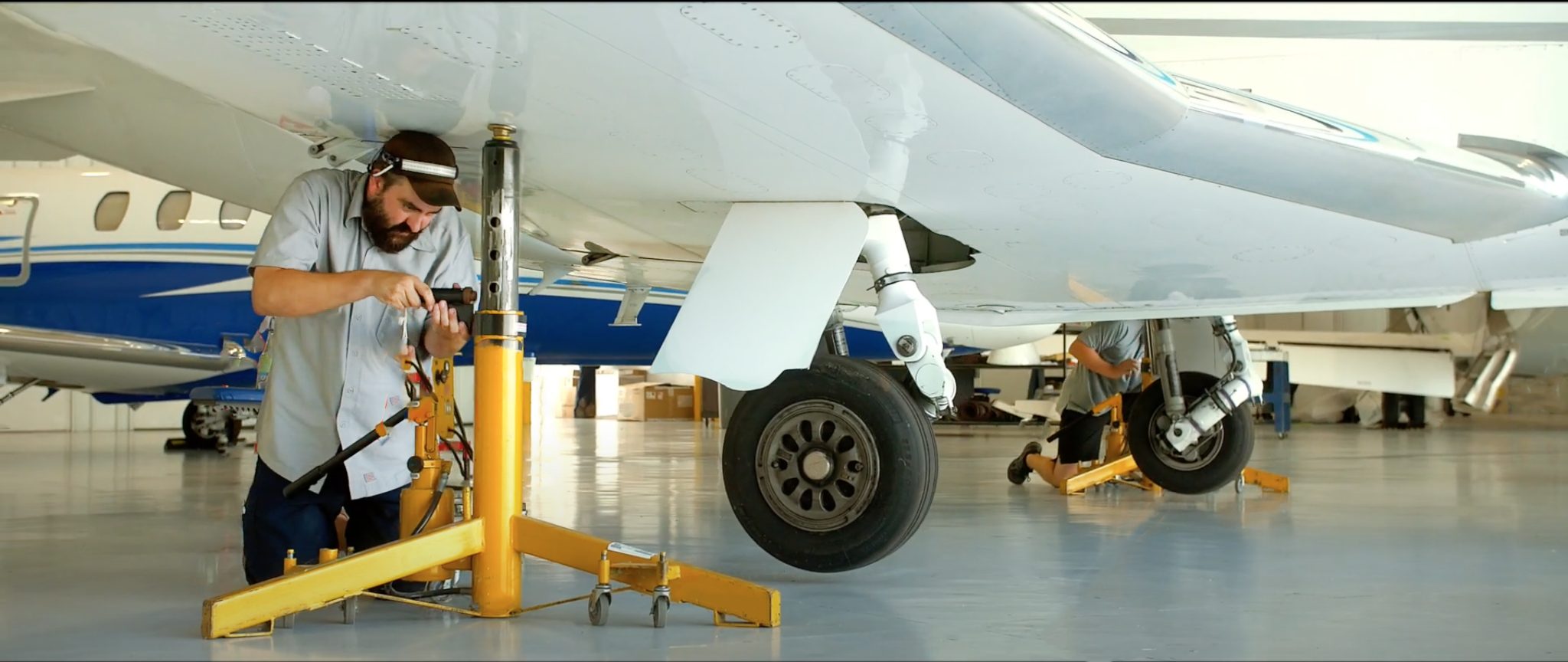 A flyExclusive technician working beneath a jacked aircraft in the hangar